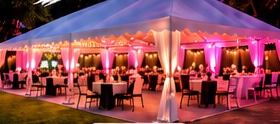 A 20 by 40 tent glowing with pink uplighting over round tables on a lawn